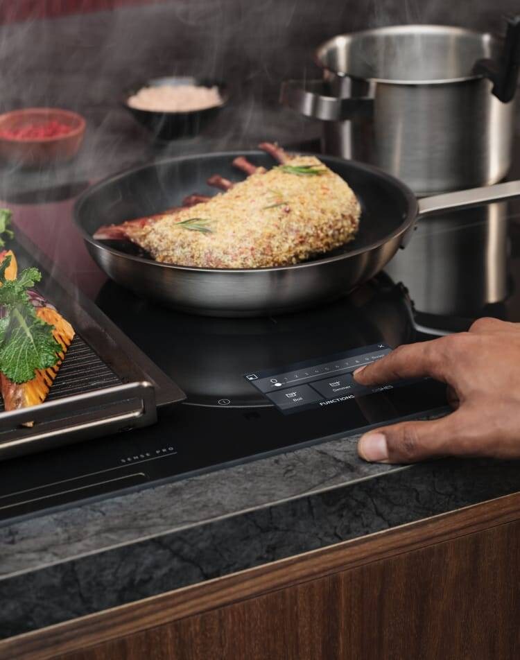 Un dito tocca il pannello di controllo di un piano cottura a induzione mentre si prepara il cibo.